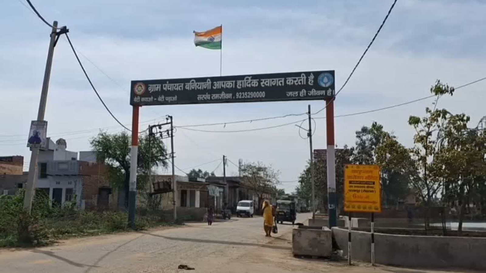 پولیس اسٹیشن کا داخلی راستہ، ہندوستانی پرچم کے ساتھ، دیہی علاقے میں سڑک اور لوگ۔.