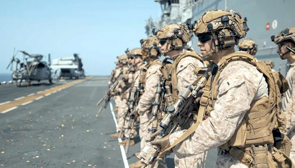 فوجی اہلکاروں کی لائن میں کھڑے ہونے کی تصویر، فوجی یونیفارم میں، ہتھیاروں کے ساتھ، سمندر کے کنارے پر.