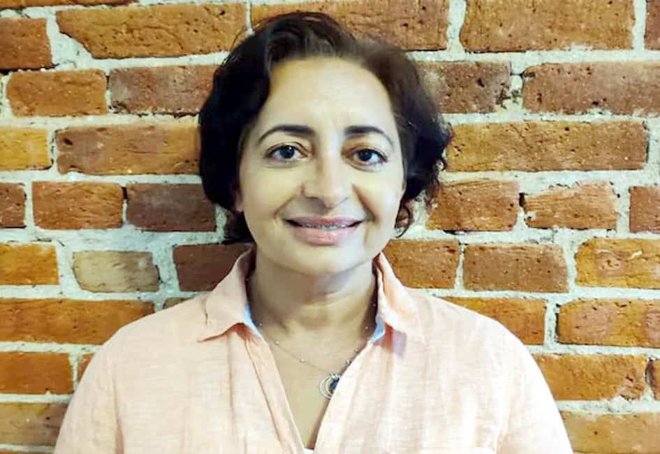 خاتون کی مسکراہٹ اور دوستانہ انداز، پس منظر میں اینٹوں کا دیوار.