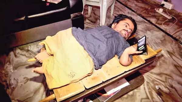 ہنستا ہوا شخص موبائل کے ساتھ لیٹا ہوا، آرام دہ ماحول میں تفریحی لمحے گزار رہا ہے۔.