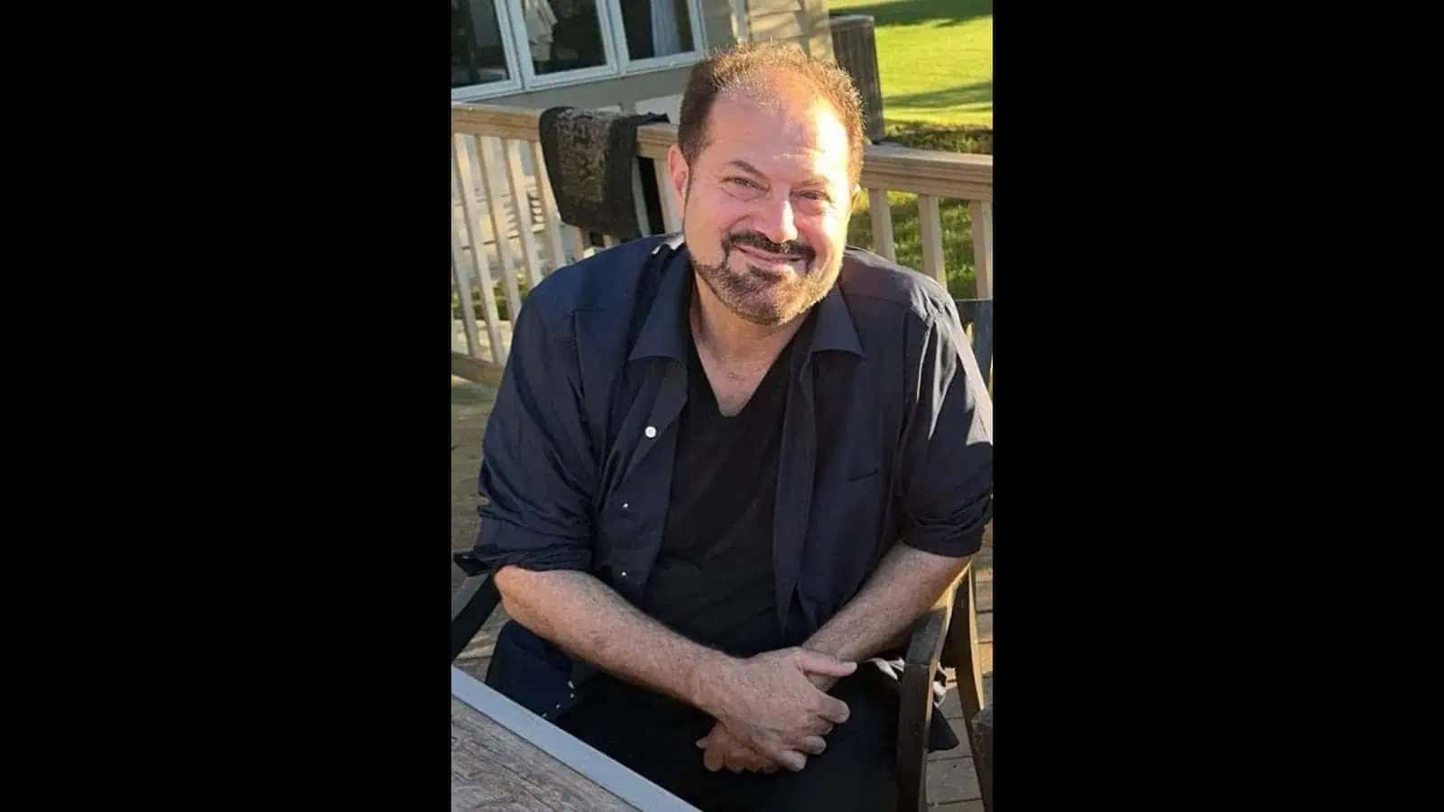 خوشگوار مرد مسکراہٹ کے ساتھ بیٹھا ہوا، آرام دہ ماحول میں، قدرتی روشنی میں، دوستانہ اور مثبت تاثرات ک.