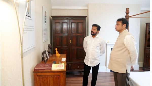 دو مرد ایک کمرے میں بات چیت کر رہے ہیں، ایک میز پر تصویریں اور اشیاء رکھی ہیں.