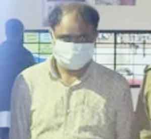 مذکورہ شخص ماسک پہنے ہوئے، باہر کھڑا ہے، پس منظر میں سڑک اور لوگ.